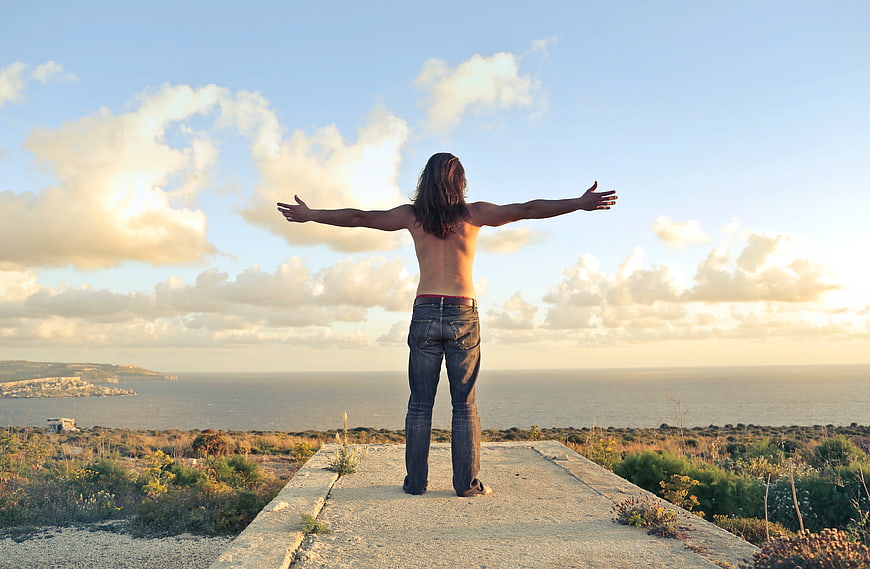 Man with arms outstretched overlooking ocean sunset