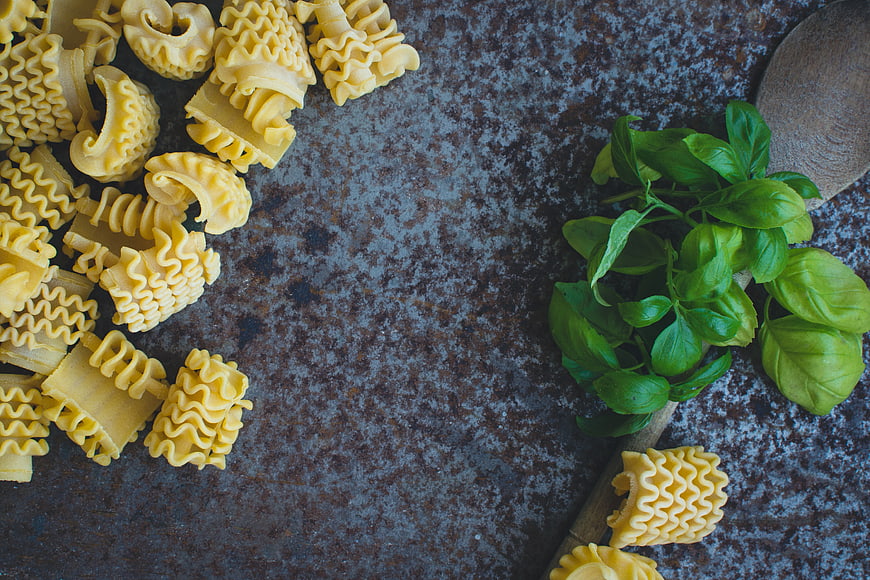 Top view of uncooked pasta shells with fresh basil and wooden spoon