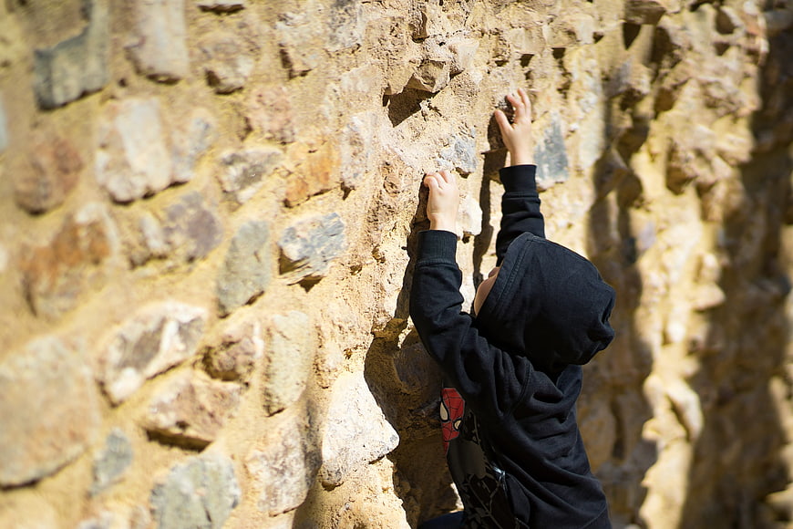 Young child climbing a textured stone wall outdoors