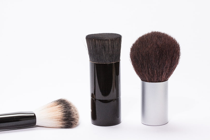 Three makeup brushes with black and silver handles on white background
