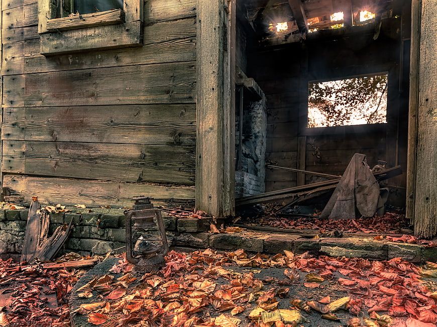 Abandoned wooden cabin interior with autumn leaves and lantern