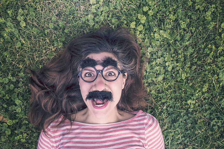 Woman with fake mustache and glasses lying on grass