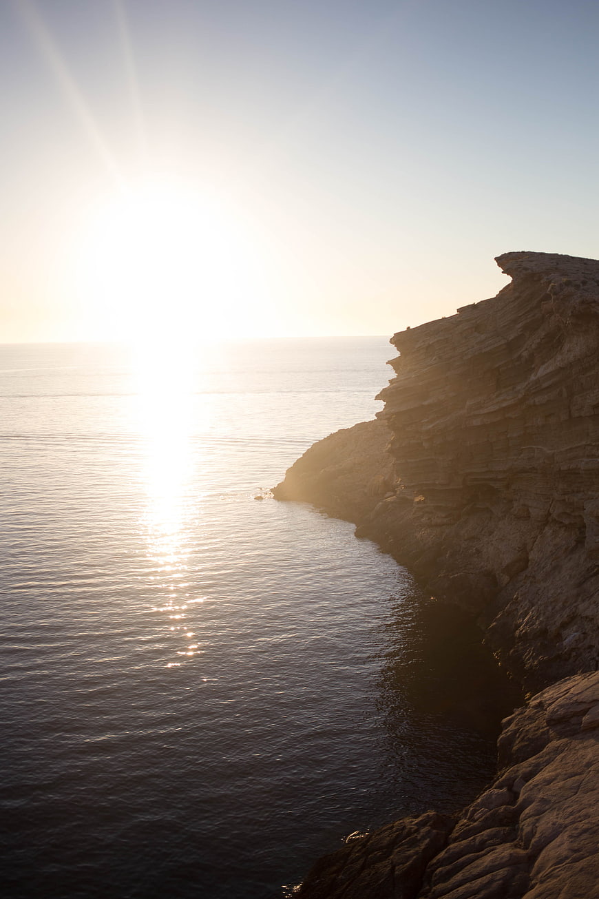 Sunset over rocky coastal cliffs and calm ocean water