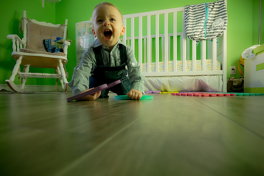 Happy toddler playing with foam puzzle on nursery floor