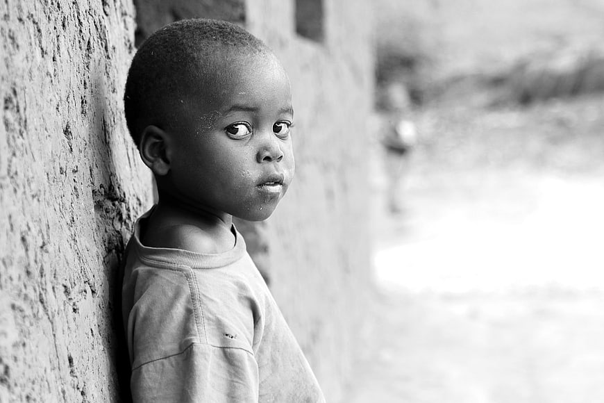 Black and white portrait of young African boy leaning against wall