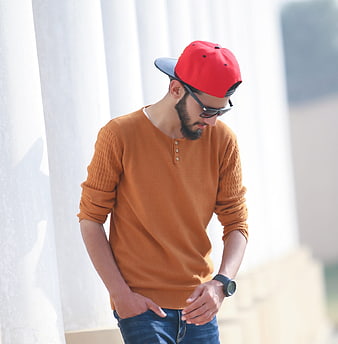 Stylish man in orange sweater and red cap posing outdoors