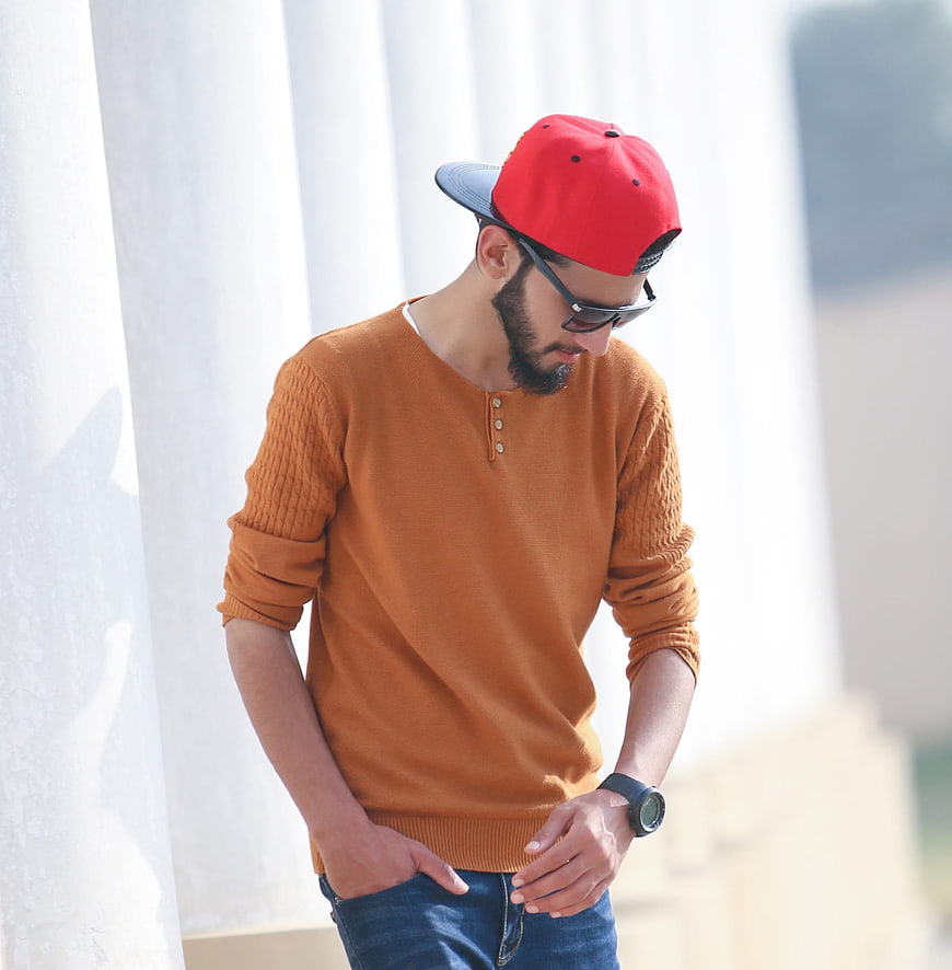 Stylish man in orange sweater and red cap posing outdoors
