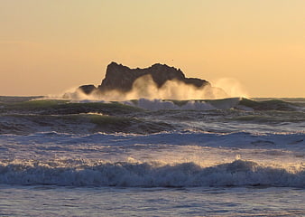 Dramatic Ocean Waves Crashing Against Rocky Outcrop at Sunset