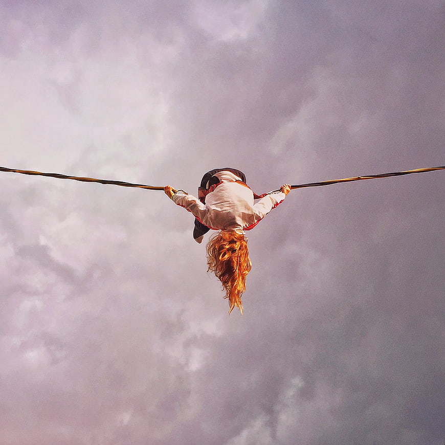 Woman Hanging Upside Down on Rope Against Cloudy Sky