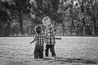 Two young boys in plaid shirts playing together in a grassy field