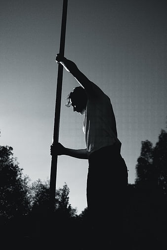 Silhouette of Man Holding Vertical Pole Outdoors