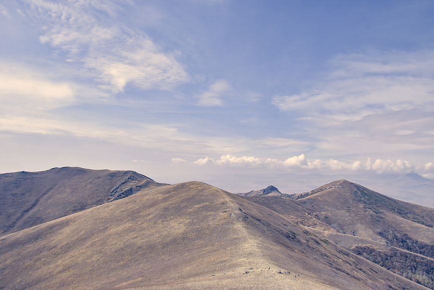 Rolling brown mountain ridges under a blue sky with clouds