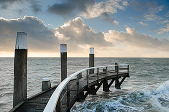 Wooden pier extending into ocean with dramatic cloudy sky