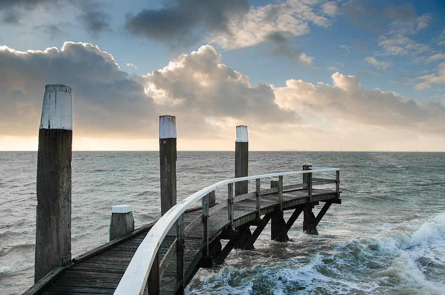Wooden pier extending into ocean with dramatic cloudy sky