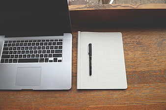 Top view of laptop, notebook, and pen on wooden desk
