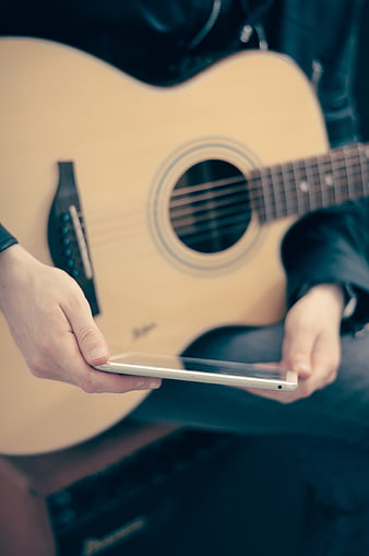 Musician holding tablet with acoustic guitar in background