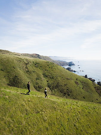 Couple hiking on grassy coastal trail with ocean view