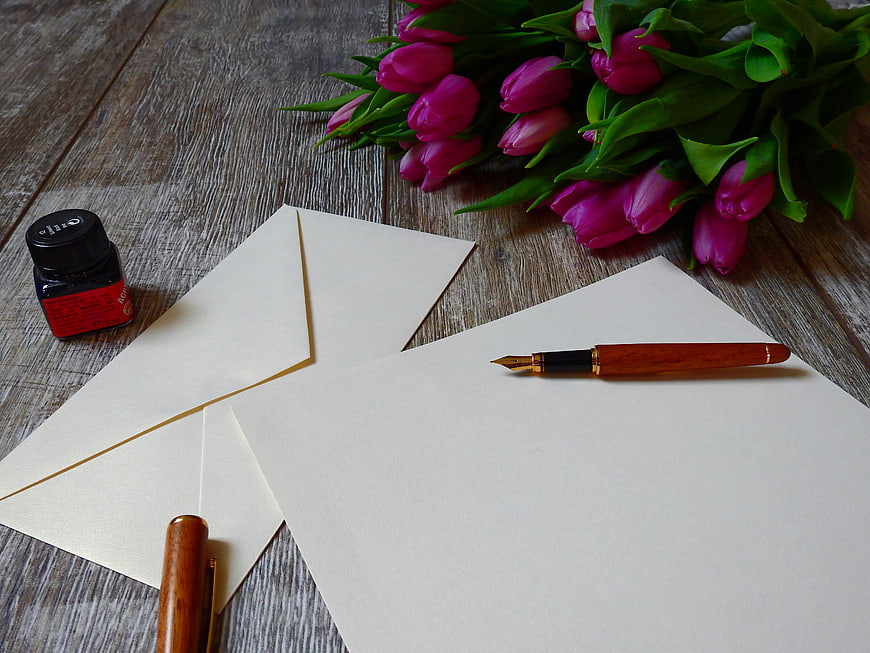 Fountain pen, ink, and pink tulips on wooden table