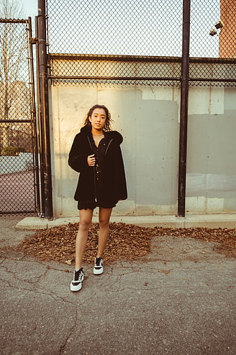 Young woman in black coat standing by urban fence