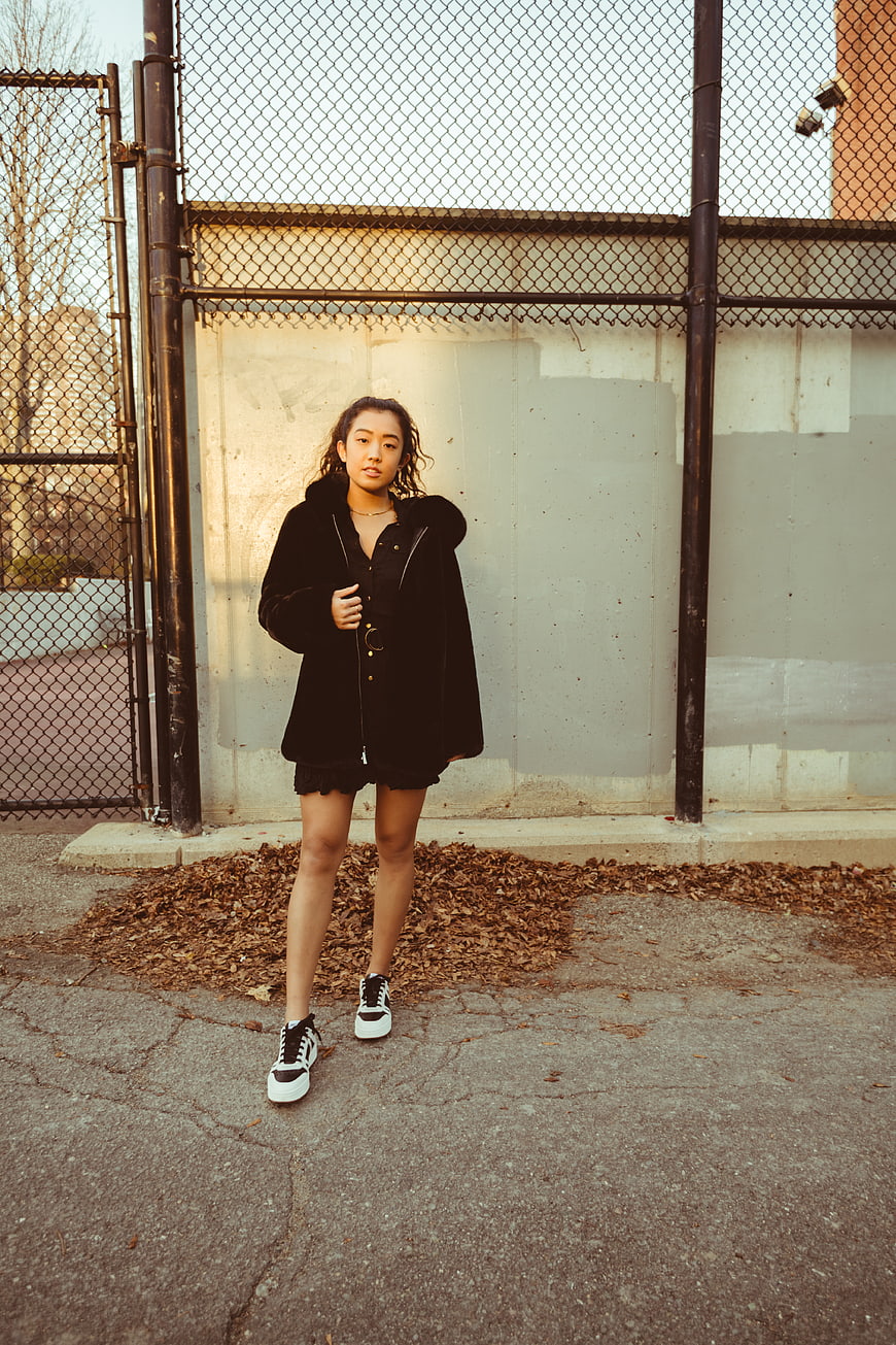 Young woman in black coat standing by urban fence
