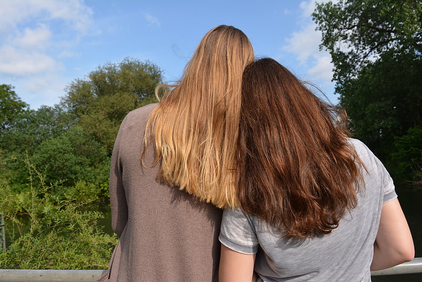 Two women with long hair leaning heads together outdoors