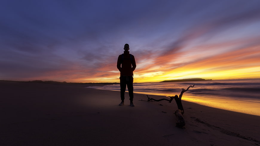 Man standing on beach at sunset with colorful sky