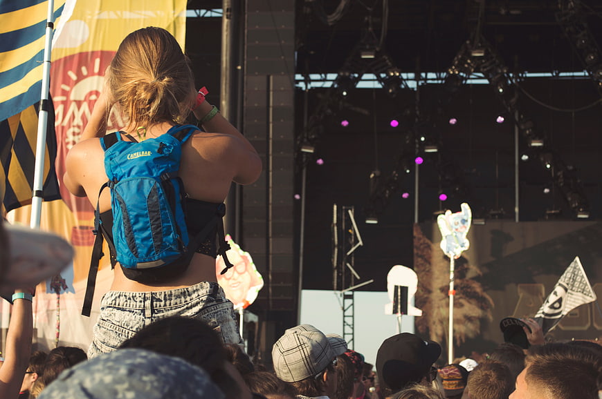 Woman with backpack on shoulders at music festival crowd