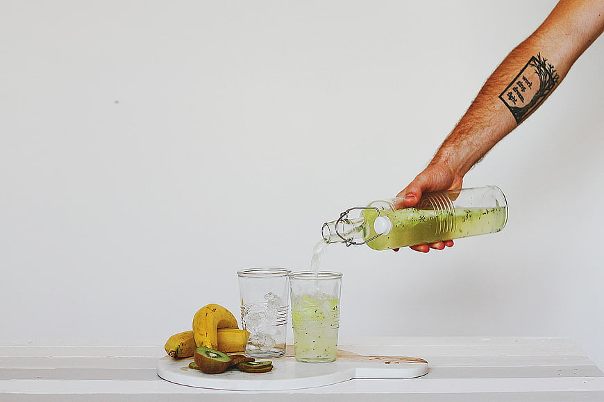 Hand Pouring Green Kiwi Banana Smoothie into Glass