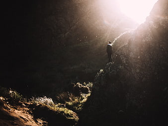 Man standing on rocky cliff edge in dramatic sunlight