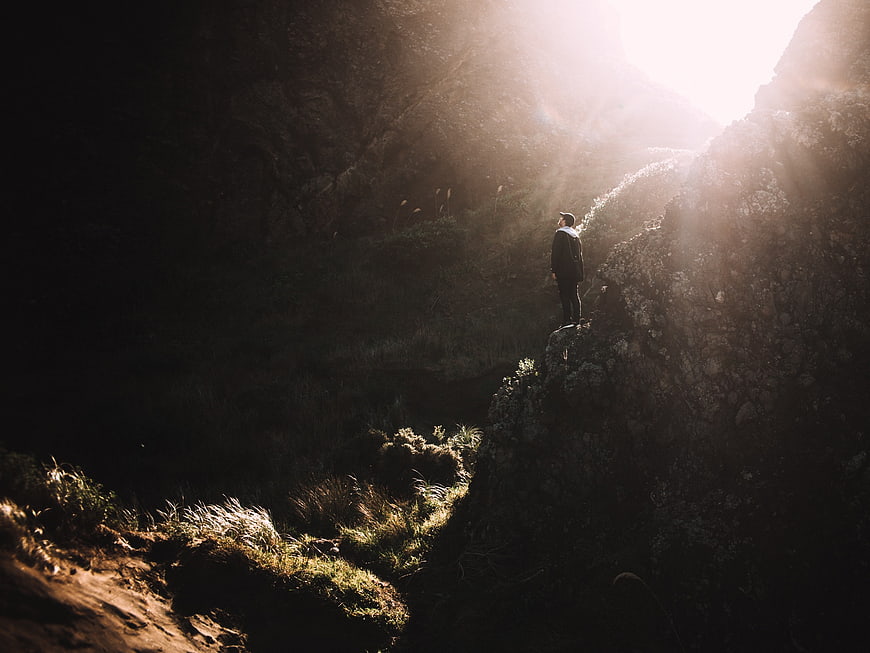 Man standing on rocky cliff edge in dramatic sunlight
