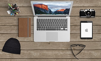 Flat lay workspace with laptop, tablet, camera, notebook, and accessories on wooden desk