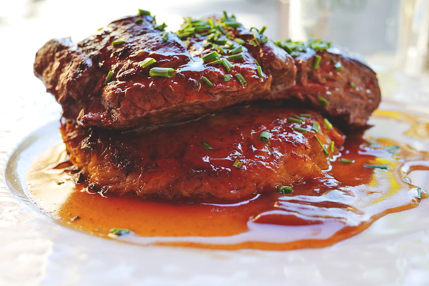 Close-up of glazed steak with sauce and chives on white plate