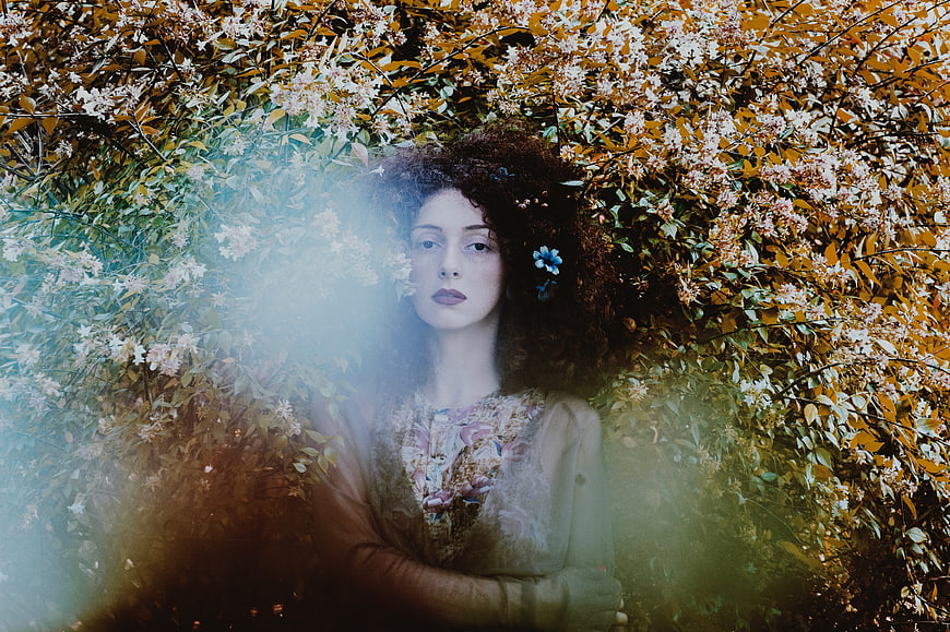 Woman with curly hair in floral bush with dreamy light leak