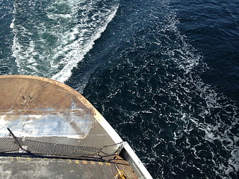 High angle view of rusty ship bow cutting through deep blue ocean water