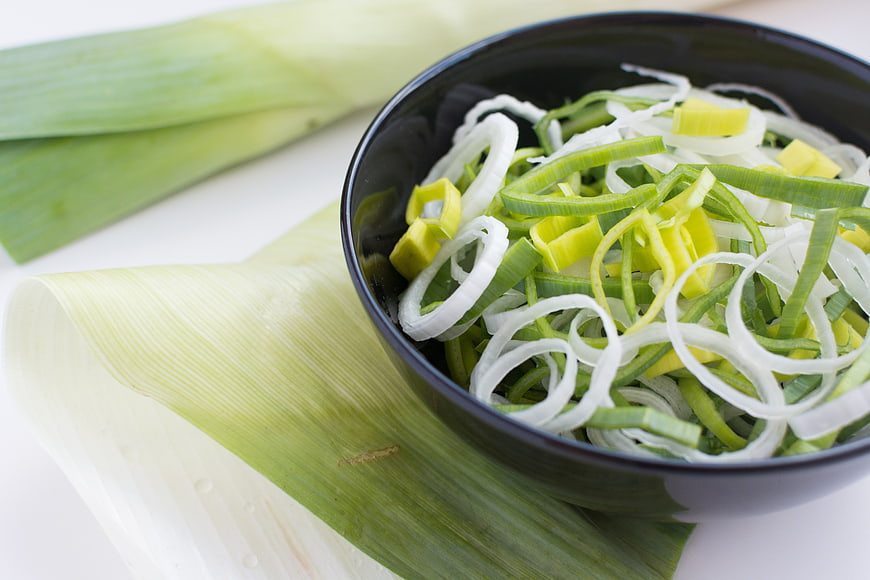 Fresh Sliced Leeks in Black Bowl on White Background