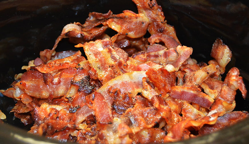 Crispy fried bacon strips in a black slow cooker pot