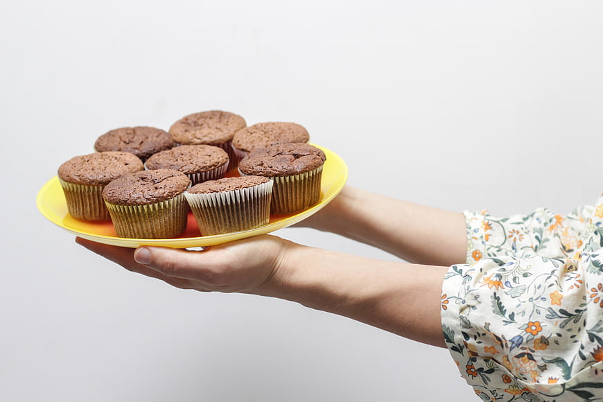 Hands holding yellow plate of chocolate muffins on white background