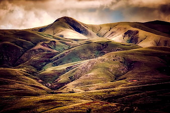 Dramatic rolling hills landscape with moody clouds and golden light