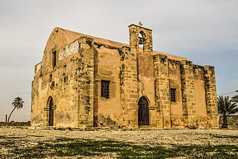 Ancient stone church in Cyprus with bell tower and palm trees