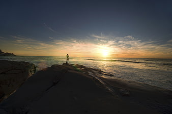 Silhouette of Man Standing on Rocky Coast at Sunrise