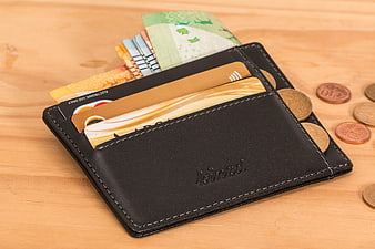Black leather wallet with cash and coins on wooden table