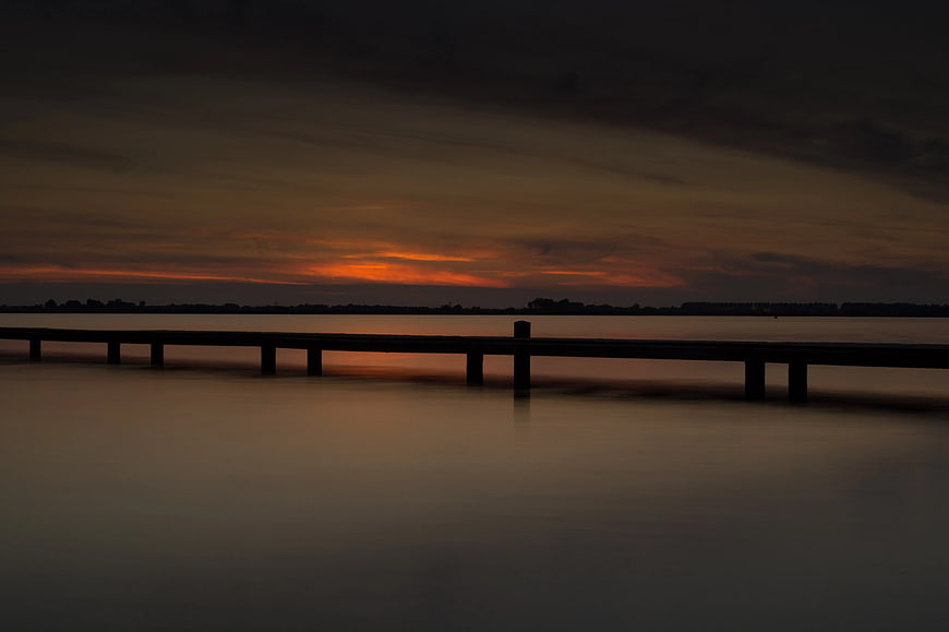 Silhouette of wooden pier at sunset over calm water
