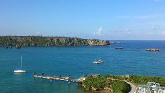 Tropical coastal landscape with pier, boats, and cliffs