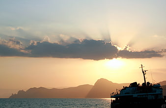 Silhouette of boat against sunset with sun rays over mountains