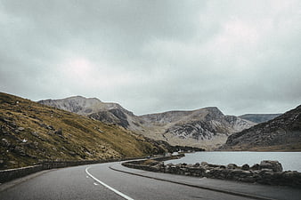 Winding Mountain Road Beside Lake Under Overcast Sky