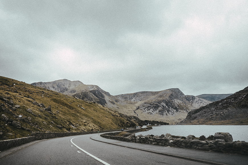 Winding Mountain Road Beside Lake Under Overcast Sky