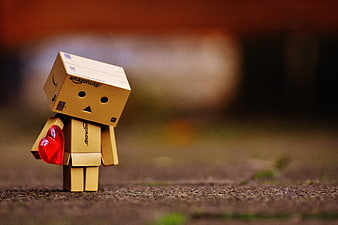 Danbo cardboard character holding red heart on textured ground
