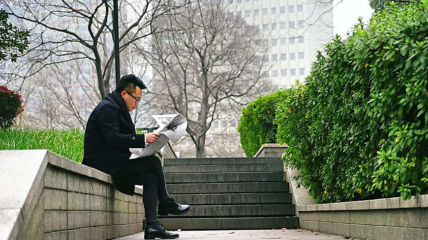 Man reading newspaper on urban park steps