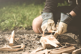 Person carving wood with knife outdoors wearing gloves