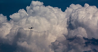 Airplane flying in front of large white cumulus clouds against a deep blue sky